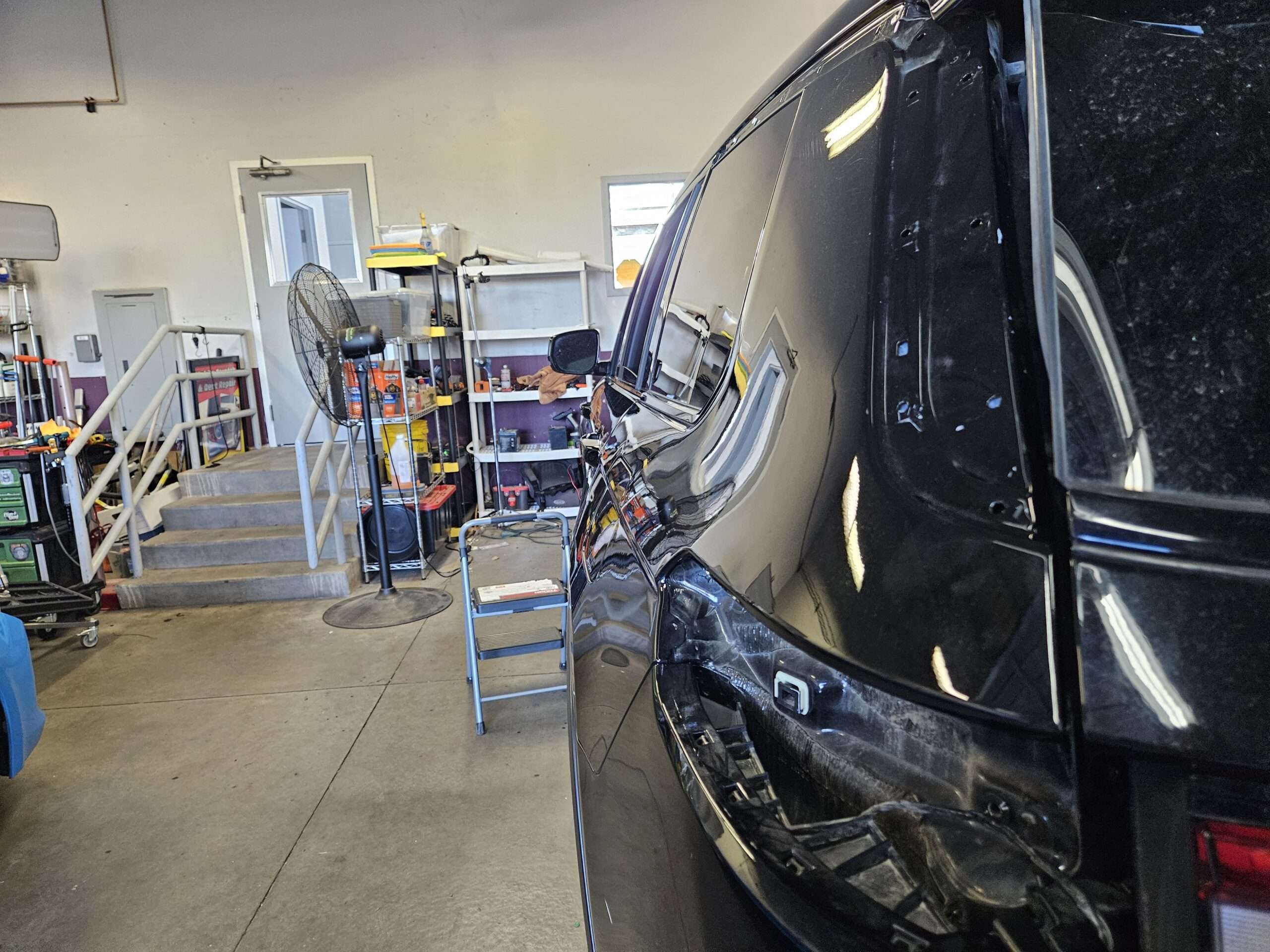 men working on a white automobile for hail damage in a shop denver colorado