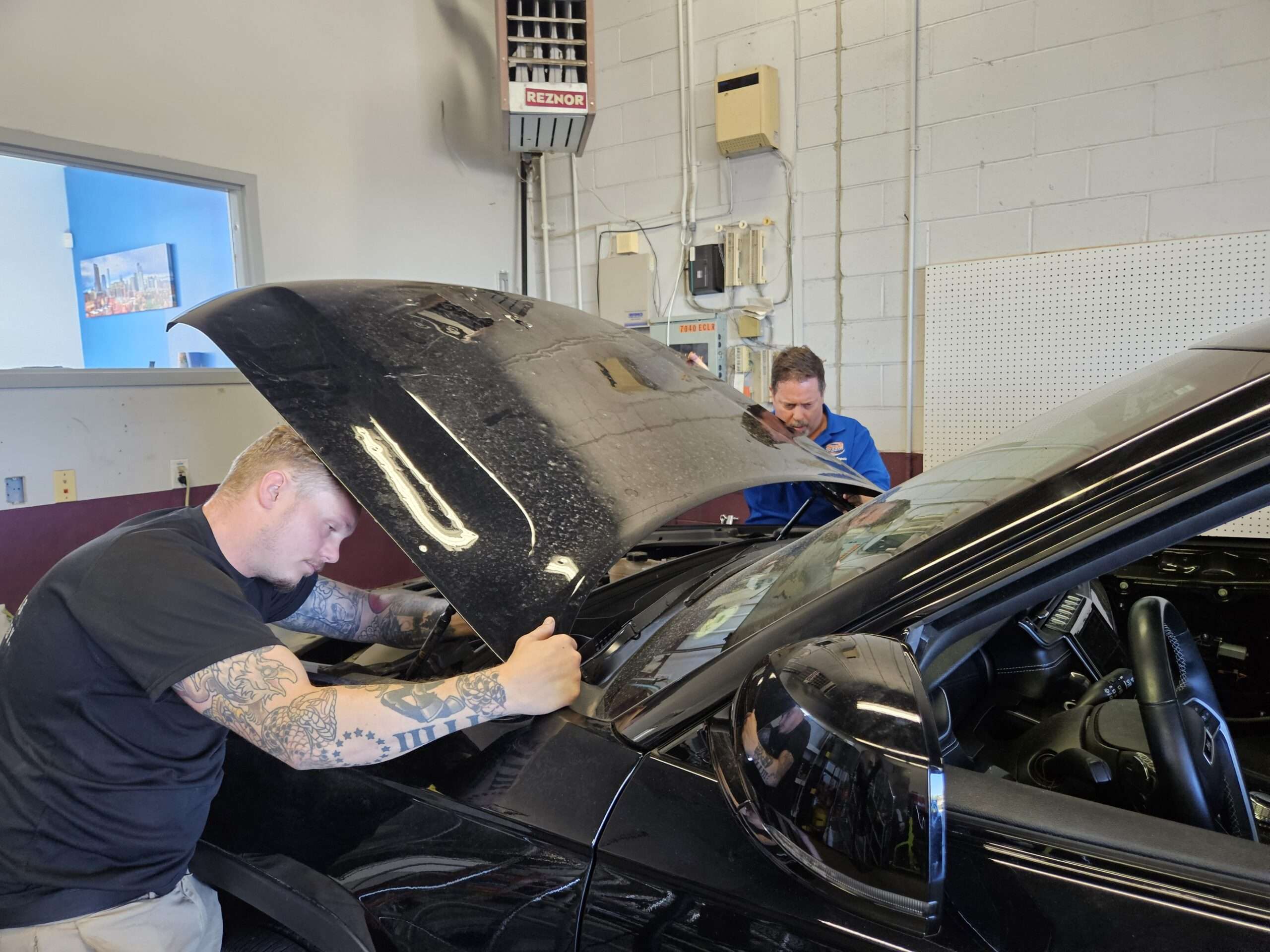 men working on a white automobile for hail damage in a shop denver colorado