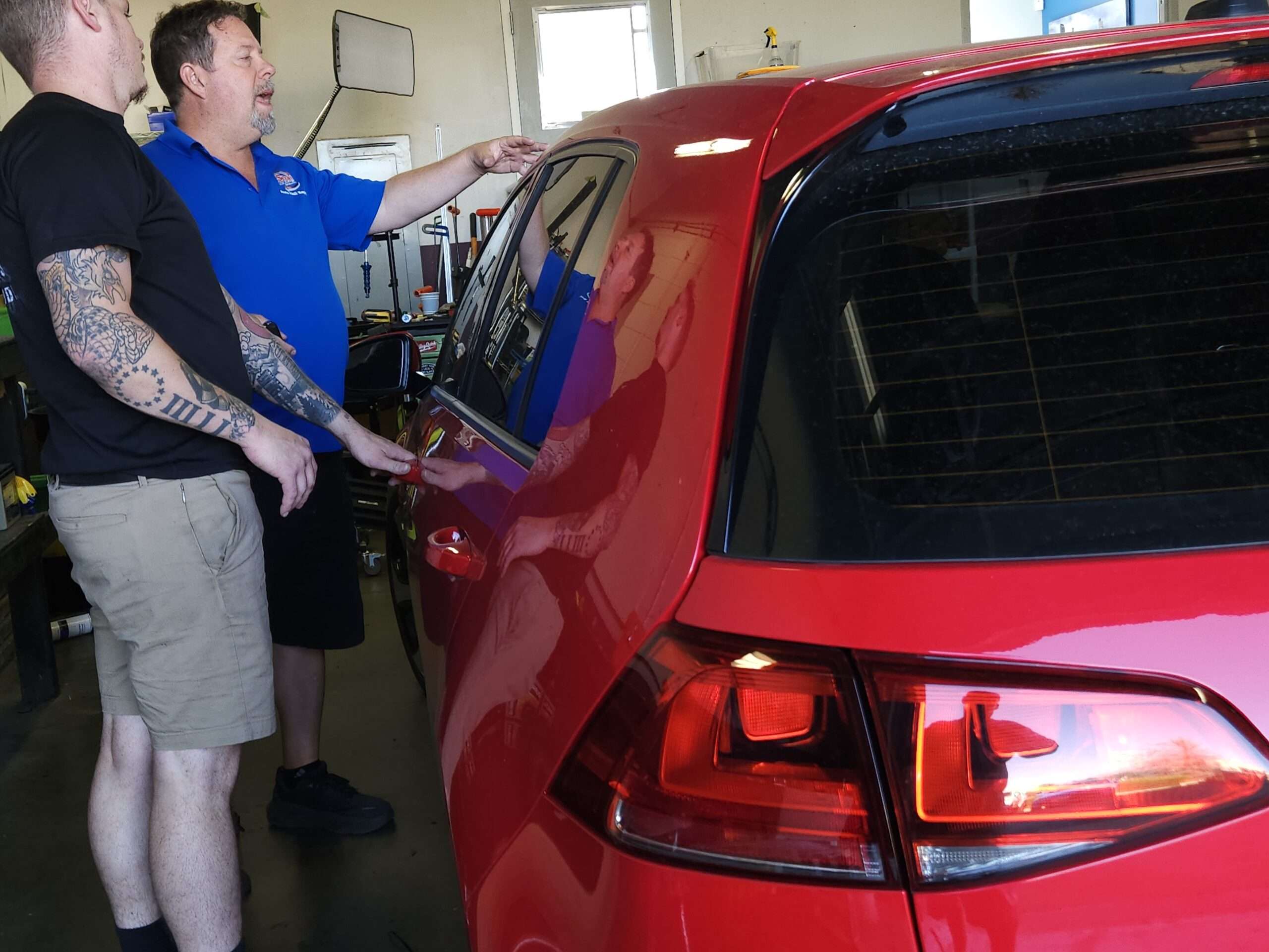 men working on a white automobile for hail damage in a shop denver colorado